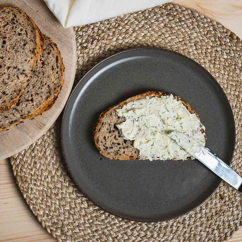 Eine Scheibe Leinenbrot mit Frischkäse und Kräutern. Perfekt zu den Leinensamen. Ein leckeres Rezept. Der Teller gibt einen tollen dunklen Kontrast.